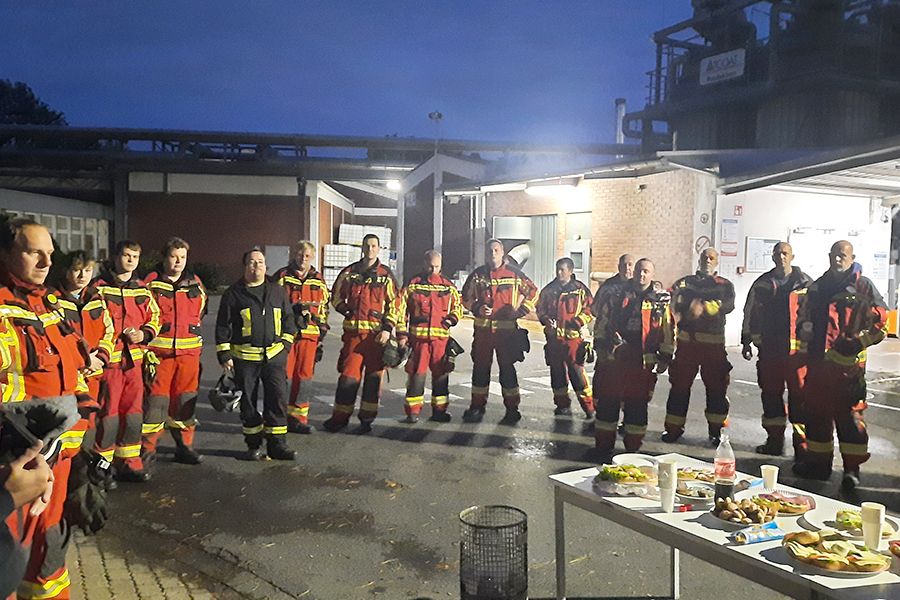 Abendliche Stimmung. Das gesamte Team der Feuerwehrleute steht bei einer abschließenden Jause zusammen.